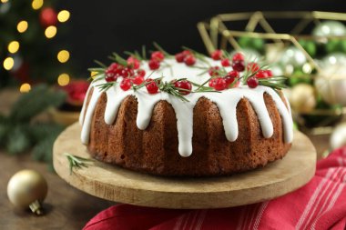 Üzerinde krema, kızılcık ve biberiye olan nefis bir Noel pastası. Siyah arka planda, bulanık ışıklarla, yakın plan. Bokeh etkisi