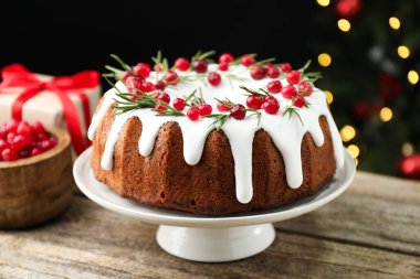 Üzerinde krema, kızılcık ve biberiye olan nefis bir Noel pastası. Siyah arka planda, bulanık ışıklarla, yakın plan. Bokeh etkisi