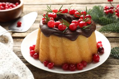 Çikolata kaplı lezzetli Noel pastası, kızılcık, biberiye ve köknar ağacı dalları ahşap masada, yakın plan.