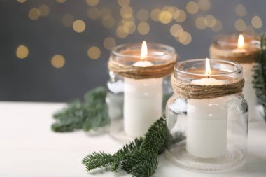 Noel fenerleri. Cam kavanozlarda mum yakmak ve beyaz masada köknar ağacı dalları bulanık ışıklara karşı, yakın çekim