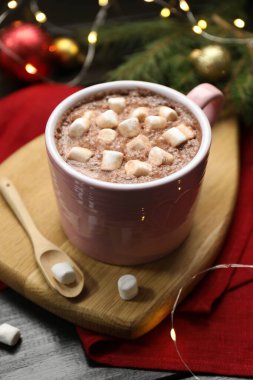 Lezzetli sıcak kakao içeceği bardakta marşmelov ve karanlık ahşap masada Noel dekoru.