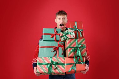 Kırmızı arka planda bir sürü hediye kutusu olan duygusal bir adam. Mutlu Noeller ve mutlu yıllar.