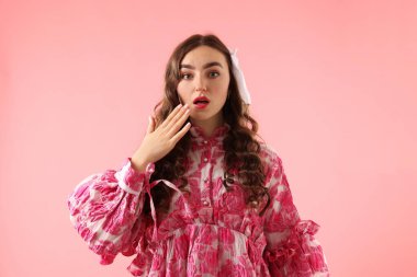 Pembe arka planda poz veren güzel giyimli genç bir kadın.