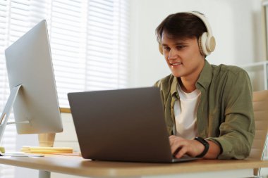 Ofisteki bilgisayarda çalışan kulaklıklı gülen programcı.