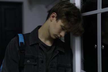 Dolabın yanında sırt çantalı depresif bir genç çocuk var.