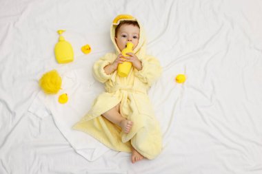 Yatakta banyo aksesuarları ve bornozlu şirin bir bebek.