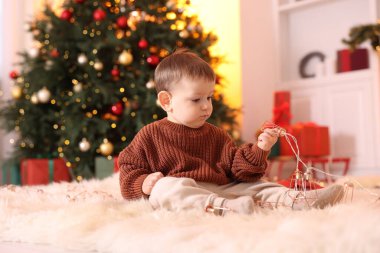 Noel için dekore edilmiş odada yerde oturan sevimli küçük bebek.