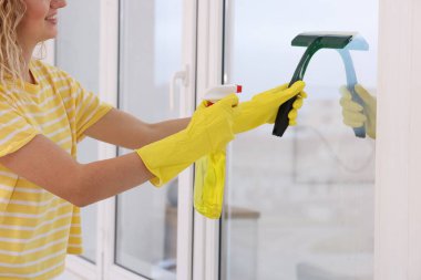 Woman cleaning window with squeegee and detergent at home, closeup