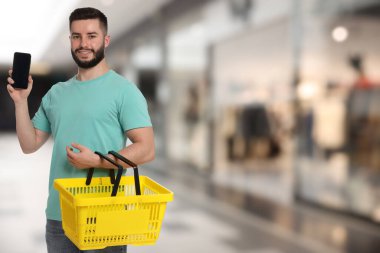 Süpermarkette elinde boş alışveriş sepeti ve cep telefonu tutan bir adam.