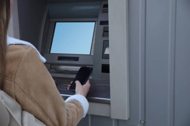 Akıllı telefonu olan bir kadın nakit para makinesi kullanıyor, yakın plan. ATM