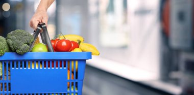 Customer holding shopping basket with different food products at supermarket, closeup. Banner design