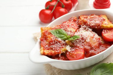 Beyaz ahşap masada domates soslu, peynirli ve fesleğenli lezzetli ravioli, yakın plan. Metin için boşluk