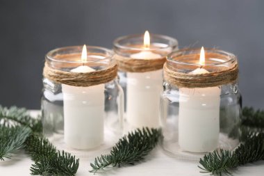 Noel fenerleri. Cam kavanozlarda mum yakmak ve beyaz masada köknar ağacı dalları ile gri arka plan, yakın plan