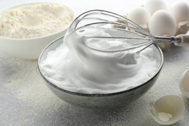 Yumurta beyazlarını kasede çırpmak, çırpmak, yumurta kabuğu ve unu gri desenli masada, yakın plan.