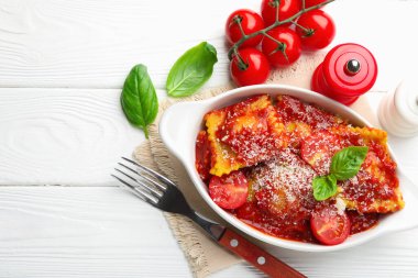 Beyaz ahşap masada servis edilen, domates soslu, peynirli ve fesleğenli ravioli. Metin için boşluk