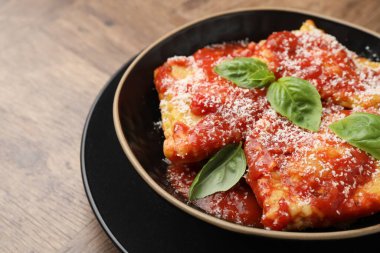 Ahşap masada domates soslu, peynirli ve fesleğenli lezzetli ravioli.