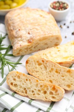 Taze kesilmiş ciabatta, biberiye ve biberiyeler gri desenli masada, yakın plan.