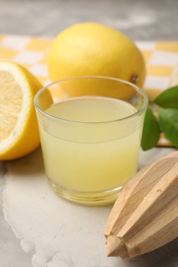 Bardakta limon suyu, sıkma, yapraklar ve açık gri masada taze limonlar. Yakın plan.