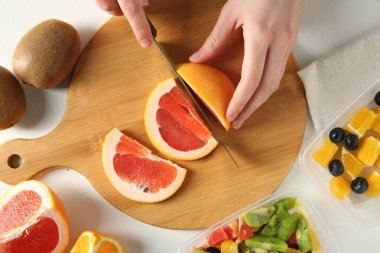 Meyve salatası yapıyorum. Beyaz masada greyfurt kesen kadın, üst manzara.