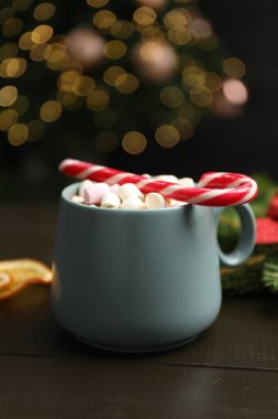 Lezzetli sıcak kakao marşmelovlu, ahşap masada şeker kamışı bulanık Noel ışıklarına karşı, yakın çekim