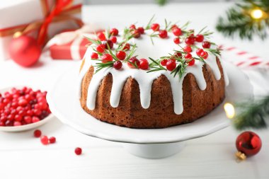 Beyaz ahşap masada kremalı, kızılcıklı ve biberiyeli lezzetli bir Noel pastası.