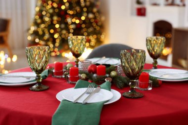 Şenlikli bir odada tabaklar, bardaklar ve mumlarla süslenmiş şık bir Noel sofrası, yakın plan. Bokeh etkisi