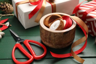 Kutlama ambalajı. Hediye kutuları, kurdeleler, makas, ambalaj kağıdı ve yeşil ahşap masa üzerindeki Noel dekoru, yakın plan.