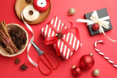 Kutlama ambalajı. Hediye kutuları, kurdele, makas, ambalaj kağıdı ve kırmızı arka planda Noel dekoru, düz yatış