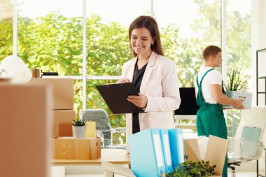 Taşınma günü. Genç adam farklı eşyaları topluyor ve ofisinde panosu olan bir kadın var.