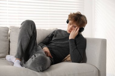 Evdeki kanepede kulaklık takan depresyondaki genç çocuk.