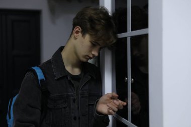 Dolabın yanında sırt çantalı depresif bir genç çocuk var.