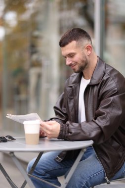 Genç adam açık kafedeki masada gazete okuyor.