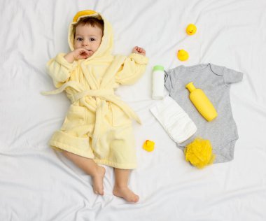 Bornozlu şirin bir bebek, banyodaki aksesuarlar ve giysiler, üst manzara.