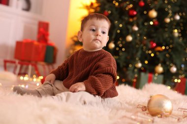 Noel için dekore edilmiş odada yerde oturan sevimli küçük bebek.