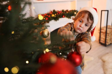 Noel Baba şapkalı küçük çocuk evde Noel ağacı süslüyor. Bokeh etkisi