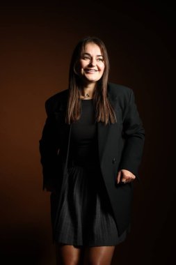 Koyu kahverengi arka planda poz veren şık elbiseli güzel bir genç kadın.