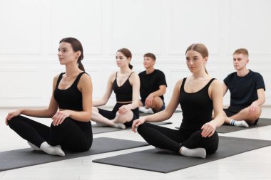 Spor salonundaki spor paspaslar üzerinde esneme egzersizi yapan bir grup insan.