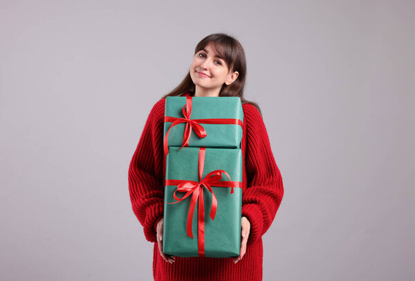 Beautiful woman in red sweater with gift boxes on grey background. Christmas and New Year celebration