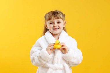 Sarı arka planda lastik ördekli bornoz giyen mutlu kız.