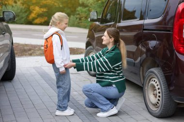Anne kızını açık hava arabasının yanına, okula götürüyor.