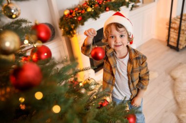Noel Baba şapkalı küçük çocuk evde Noel ağacı süslüyor, manzaranın üstünde. Bokeh etkisi