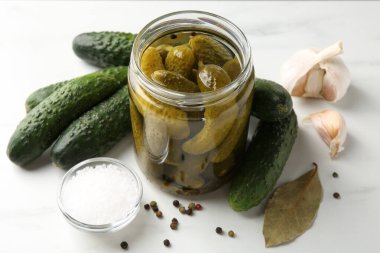 Kavanozda salatalık turşusu, beyaz masada taze sebze ve baharat, yakın plan.