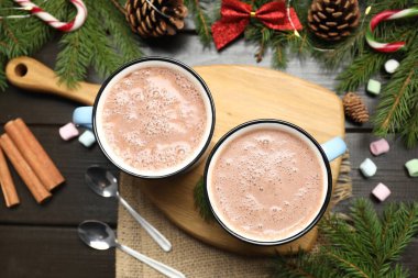 Lezzetli sıcak kakao bardakları, marşmelovlar ve karanlık ahşap masa üzerindeki Noel süslemeleri, düz yatış.