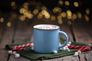 Ahşap masanın üzerinde lokum ve şeker kamışlı lezzetli kakao bulanık Noel ışıklarına karşı, yakın plan.