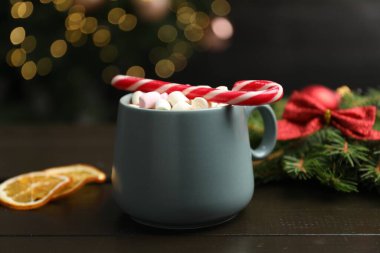 Lezzetli sıcak kakao, şekerleme kamışı, köknar ağacı dalı ve ahşap masada kurumuş portakal dilimleri bulanık Noel ışıklarına karşı, yakın çekim