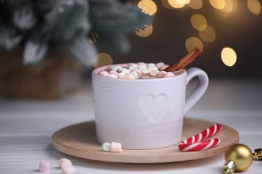 Lezzetli kakao, tarçın, şeker kamışı ve Noel süsleri beyaz ahşap masada bulanık ışıklara karşı, yakın çekim