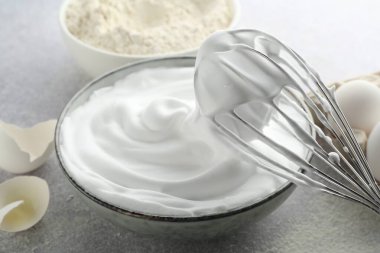Yumurta beyazlarını kasede çırpmak, çırpmak, yumurta kabuğu ve unu gri desenli masada, yakın plan.