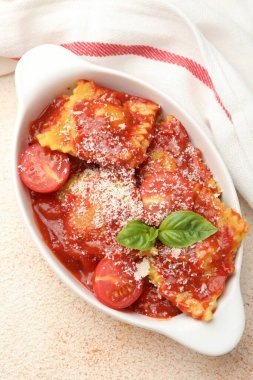 Domates soslu, peynirli ve fesleğenli ravioli hafif desenli masada, üst görünümde.