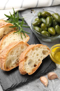 Ciabatta dilimleri, baharatlar ve zeytinler gri masada, yakın plan.