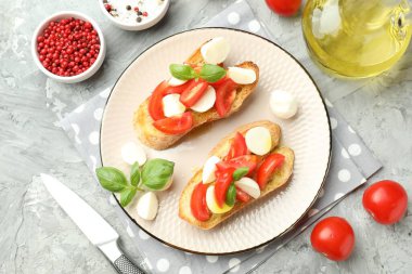 Mozarella peynirli, domatesli, fesleğenli ve baharatlı lezzetli bruschettalar gri desenli masa, düz yatak